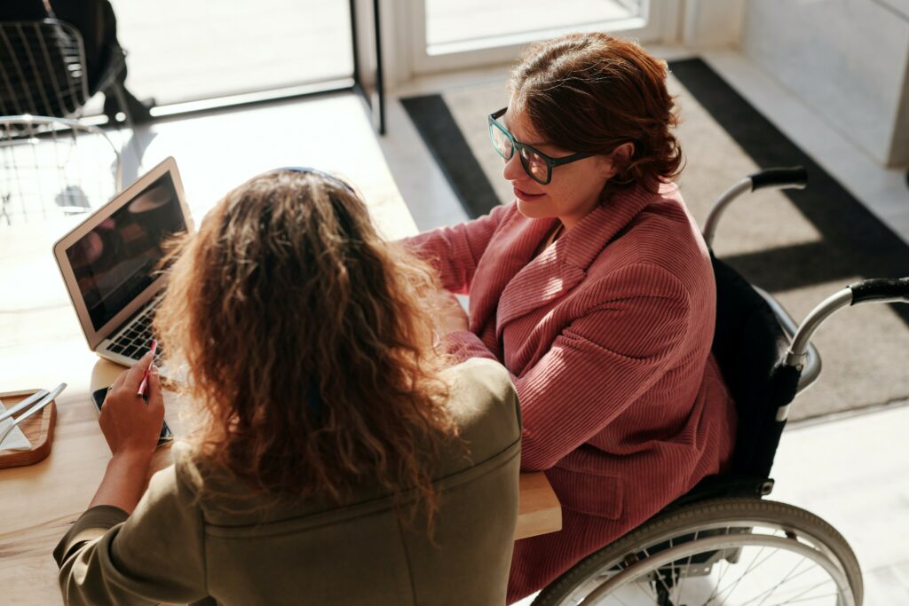 Two women working together on a project with their laptop, one woman in a wheelchair